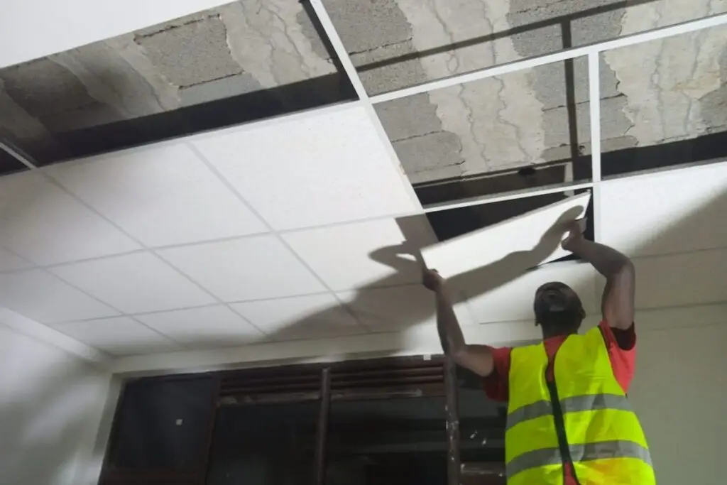 Technician installing acoustic ceiling panels in office interior