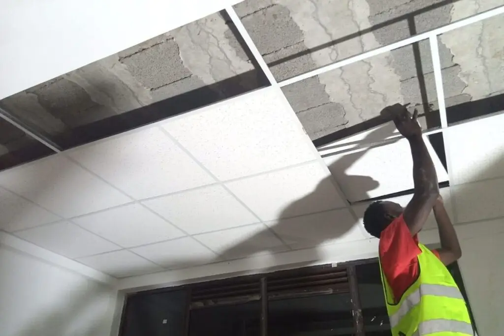 Interior worker fitting suspended acoustic ceiling in office